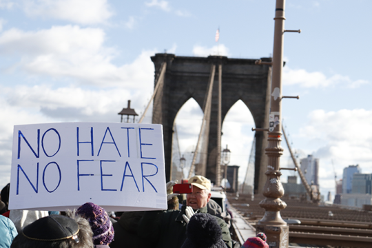 Photo of a person holding up a sign that says "NO HATE NO FEAR"