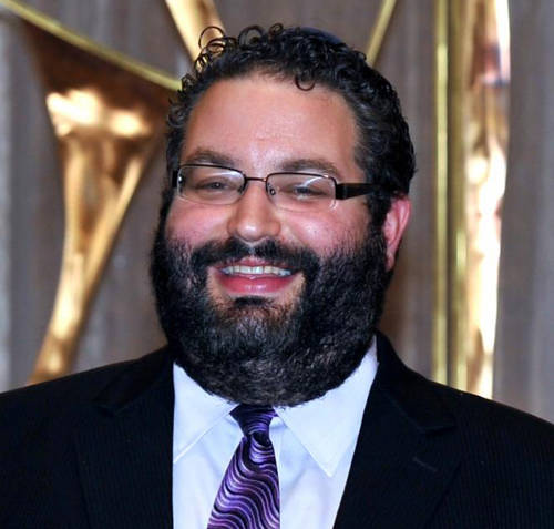 Headshot of a smiling man with glasses and a beard wearing a purple tie