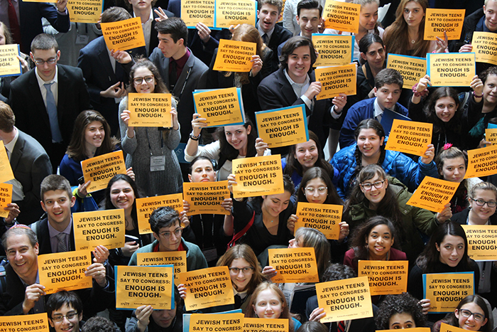 Attendees of Ltaken social justice seminar holding signs saying Jewish teens say to Congress Enough is Enough