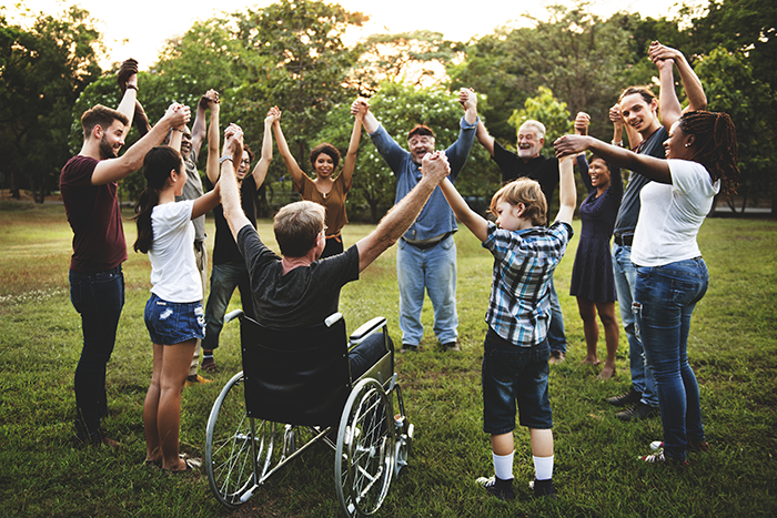 an image of a diverse group of people of different genders, ages, and race, one in wheel chair, in a group holding their hands up in the air