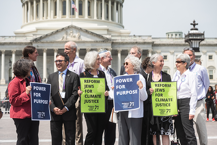 an image of a group of people standing in front of the capital building in washingtin dc holding signs that say "power for purpose" and "reform jews for climate justice"