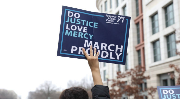 Disembodied hand holding a sign that says DO JUSTICE LOVE MERCY MARCH PROUDLY