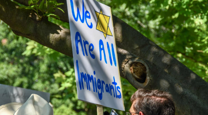 Sign reading WE ARE ALL IMMIGRANTS alongside a yellow Star of David