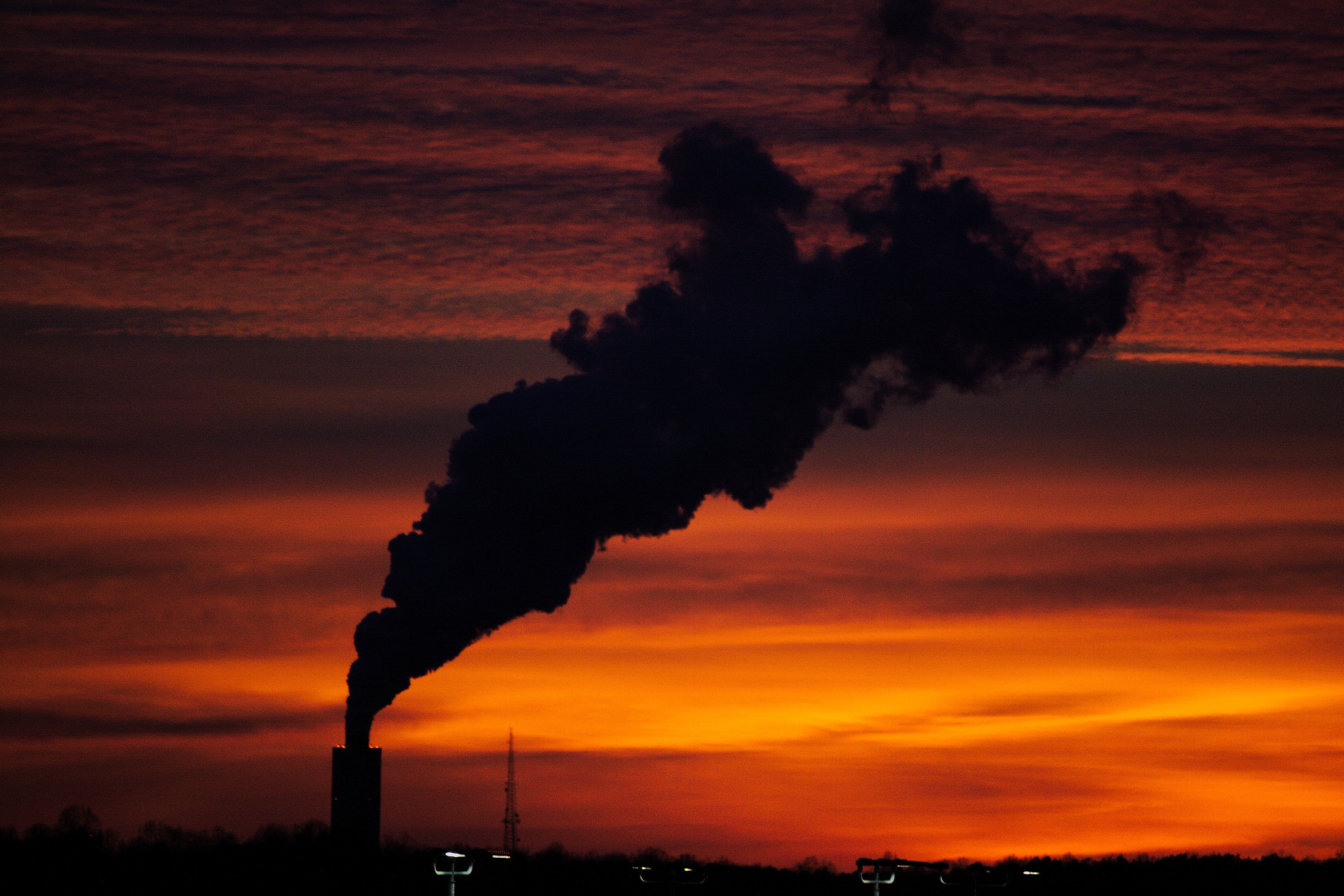 Smoke billowing from a tower against a sunset