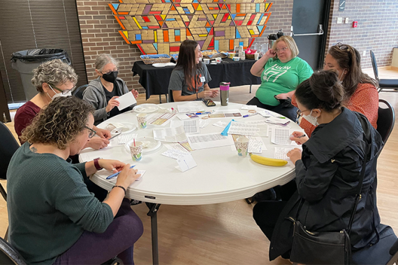 Seven people sitting at a table writing postcards