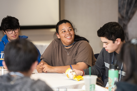 an image of a girl smiling while sitting at a table with other teenagers at L'Taken