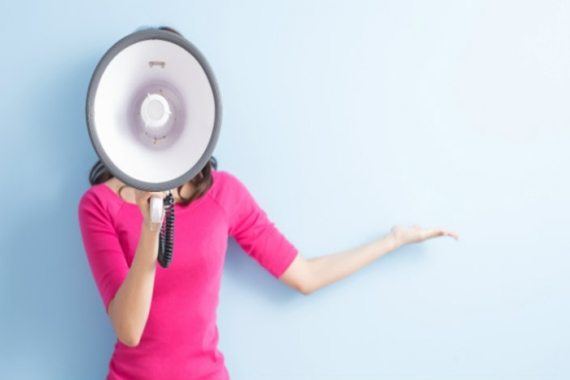 Woman in bright pink sweater (face obscured) speaking into megaphone