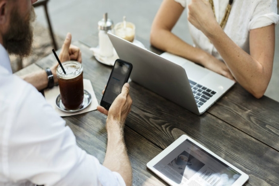 Aerial view of two individuals working together on computers surrounded by coffee and other technology