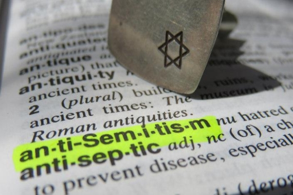 Dictionary open to the definition of antisemitism with a small metal objected engraved with a Star of David holding down the page