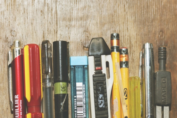 Various pens, pencils, and screwdrivers, side-by-side in front of a wooden background