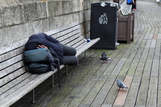 Homeless individual sleeping on a bench outdoors