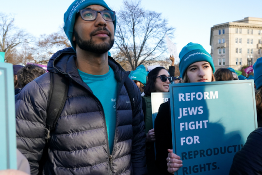 Two people standing, holding a sign that says "Reform Jews Fight for Reproductive Rights"