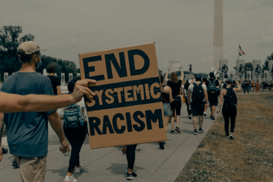 marching with a large sign saying end systematic racism 