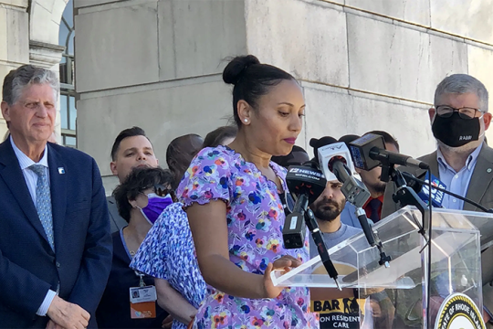 Adelina Ramos (center), a CNA at Greenville Nursing Center, addressed the crowd outside the Rhode Island State House before Gov. Dan McKee (left) signed the Nursing Home Staffing and Quality Care Act, with Temple Sinai's Rabbi Jeff Goldwasser (right) looking on.