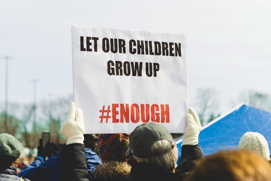 Marchers carrying a sign that says Let Our Children Grow Up - (hashtag) Enough