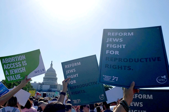 People holding up signs at a rally in front of the Capitol building in Washington D.C. Signs say Reform Jews fight for abortion rights.