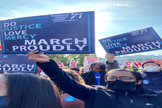 The author at a protest holding up a sign that reads "March Proudly"