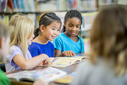an image of three young kids sitting at a table reading books