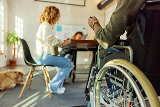 Unrecognizable man in wheelchair having a meeting at casual office with two women sitting in background