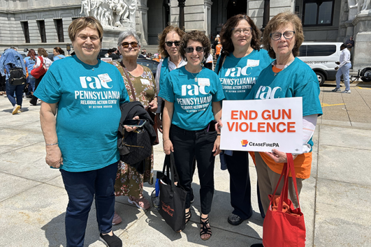 Photo of a group of people wearing RAC Pennsylvania shirts; one of them is holding a sign that says "End Gun Violence"