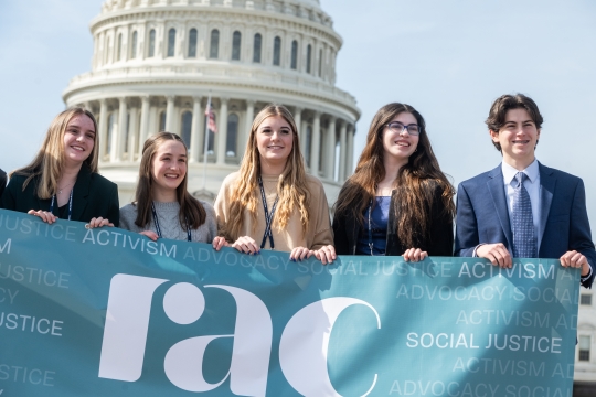 Students standing in front of the Capitol Building, holding the RAC banner.