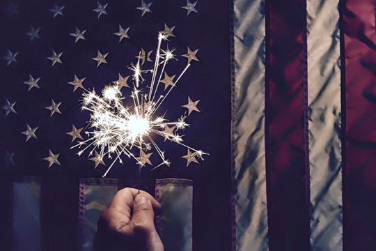 Photo of a sparkler in front of an American flag