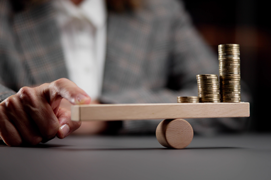 person holding finger on a fulcrum balance with coins balanced on the other side
