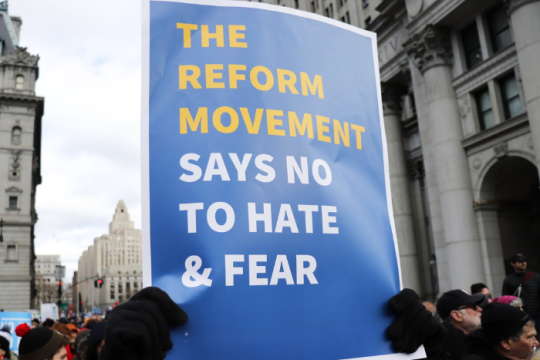 person carrying a sign that says the Reform Movement Says No to Hate and Fear
