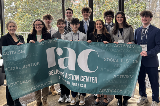 Photo of a group of students  at L'Taken lobbying about immigration; the group is holding a RAC sign