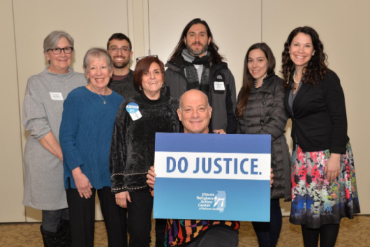 People posing for a photo with a RAC-IL sign that says "Do Justice"