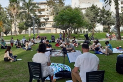 Synagogue memeber sit on the grass in a park and wear face masks during an outdoor Shabbat servicerk
