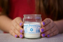 Hands with purple nail polish lightly hold a Yahrzeit candle 