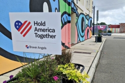 Yard sign reading HOLD AMERICA TOGETHER placed in a potted plant against a colorful mural wall