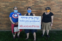 Masked protesters stand with a sign that says "Justice, Justice, You Shall Pursue" with the hashtag #BlackLivesMatter