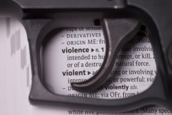 Closeup of a black handgun lying on a dictionary definition of gun violence 