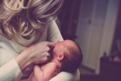 Blond mother looking down as she tries to soothe a crying baby she holds in her arms