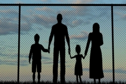 Silhouette of family members holding hands in front of a chain link fence