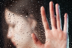 A womans blurred face behind wet glass with her hand pressing up upon the glass