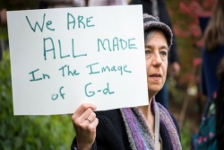Woman holding a handwritten sign that says We Are All Made in the Image of God