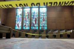 A still photo from the documentary depicting synagogue pews with yellow police tape across them and a stained window in the back