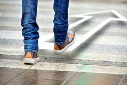 Tile floor with a pair of jean-clad legs and sneaker-clad feet taking a step forward in the direction of an arrow that is a few inches off the floor