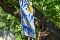 Sign reading WE ARE ALL IMMIGRANTS alongside a yellow Star of David