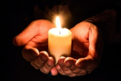 Upturned hands holding a lit candle in the darkness as in prayer or mourning