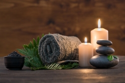 Spa towel, candles, rocks, and green leaves arrayed against a wood backdrop